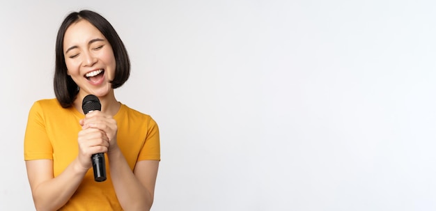 Free photo happy asian girl singing and having fun holding microphone at karaoke standing in yellow tshirt agai