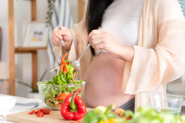 Happy asian pregnant woman cooking salad at home doing fresh green salad eating many different vegetables during pregnancy healthy pregnancy concept