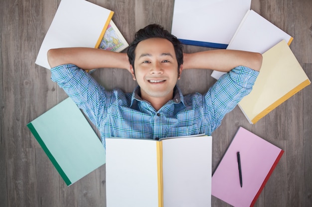 Free Photo happy asian teenage boy lying on floor among books