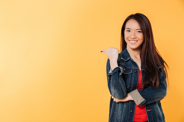 Happy asian woman in denim jacket pointing away on copyspace