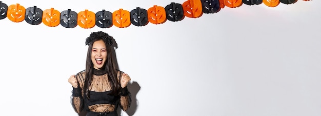 Free photo happy asian woman enjoying halloween wearing wicked witch costume and rejoicing against pumpkin stre