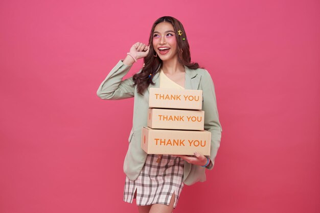 Happy Asian woman smiling and holding package parcel box isolated on pink background