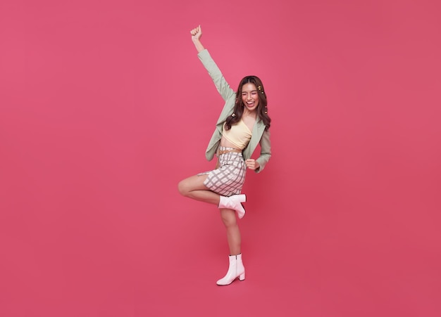 Happy Asian woman smiling and jumping while celebrating success isolated over pink background