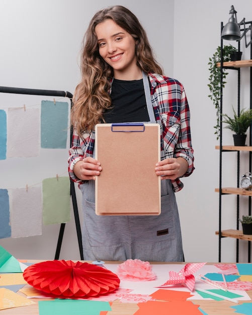 Happy attractive female artist showing clipboard with plain brown paper