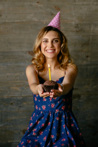 Happy attractive girl holds a chocolate cupcake with candle, celebrating her birthday