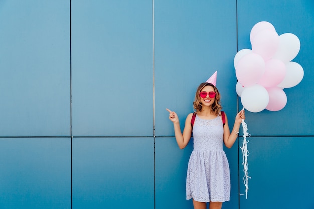 Free Photo happy attractive woman in sunglasses and party hat, holds air balloons