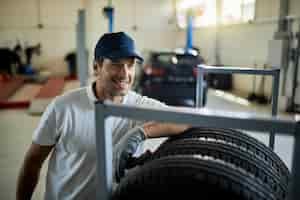 Free photo happy auto mechanic leaning on stack of car tires while working in a workshop