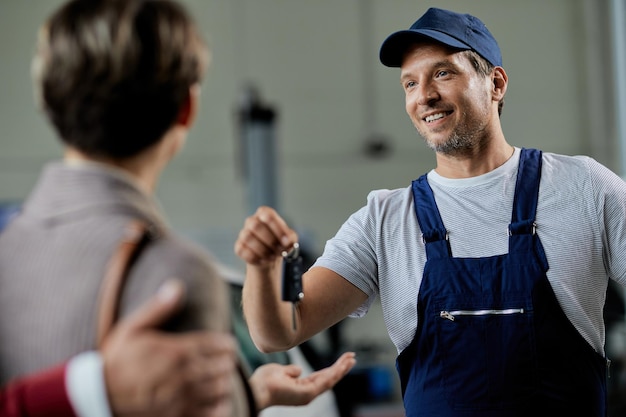 Free photo happy auto repairman handing over cark keys to his customers in a workshop