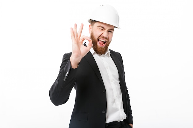 Happy bearded business man in protective helmet showing ok sign