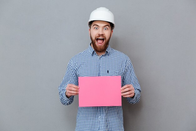 Happy bearded man builder holding blank paper