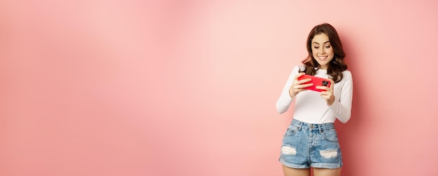 Free Photo happy beautiful girl playing mobile video game holding smartphone horizontally watching on cellphone