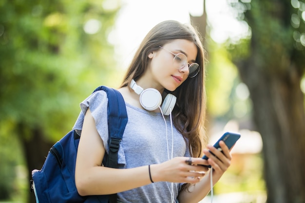 Happy beautiful young Caucasian girl with green smart phone outdoors on sunny summer day texting and smiling.