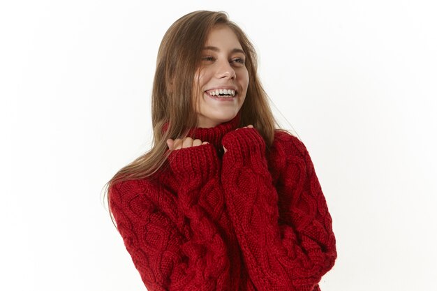 happy beautiful young female wearing maroon long sleeved sweater, smilijg joyfully. Positive friendly girl with charming broad smile, posing indoors in stylish knitted pullover