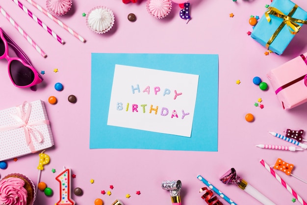 Happy birthday card surrounded with birthday items on pink backdrop