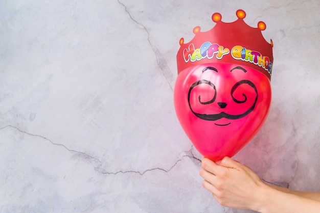 Free photo happy birthday crown on pink balloon against cracked wall