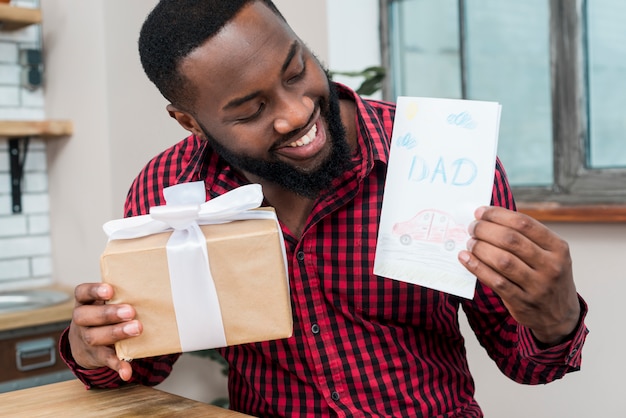 Free photo happy black man holding greeting card and gift