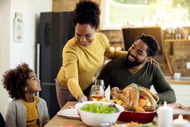 Free photo happy black mother serving salad to her family during thanksgiving meal at home