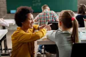 Free photo happy black teacher and schoolgirl using digital tablet in the classroom