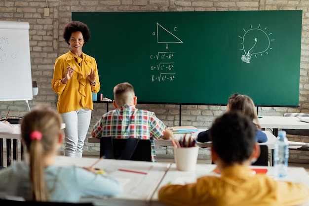 Happy black teacher talking to her students while giving math lesson in the classroom