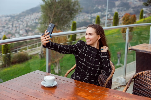 Free Photo happy blogger girl is taking selfie with her smartphone by raising up hand by sitting on city view background