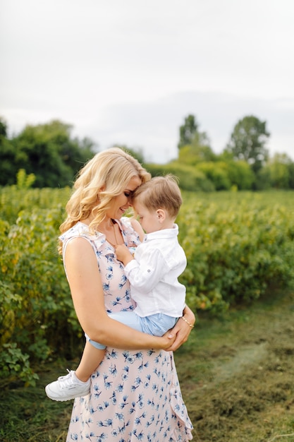 Happy blond woman and cute little boy standing in summer garden