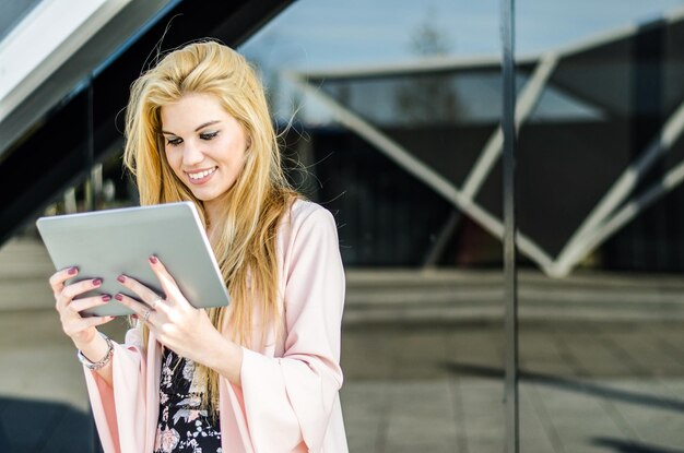 Free Photo happy blonde young woman outdoor using her tablet