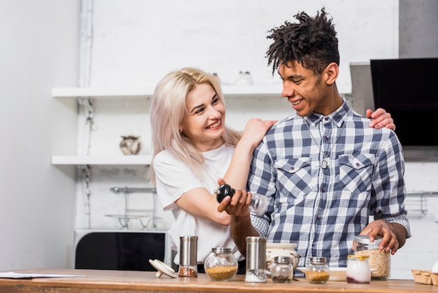 Free photo happy blonde young woman standing behind her boyfriend preparing the food in the kitchen