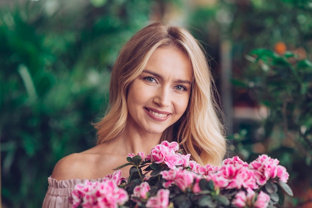 Happy blonde young woman standing behind the pink flowers with blurred background