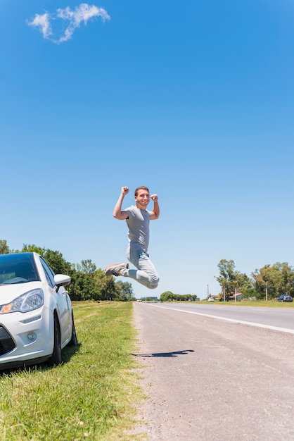 Happy boy jumping on the road next to car