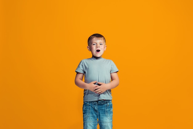 The happy boy standing and smiling against orange wall