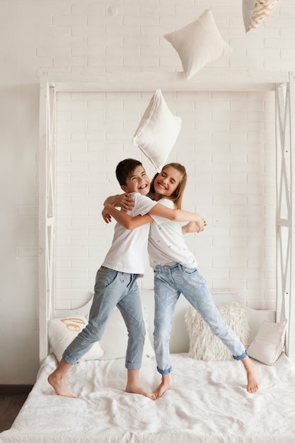 Happy brother and sister embracing on bed at home