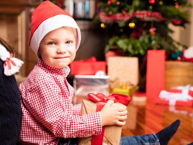 Happy brother with a christmas gift sitting on the floor