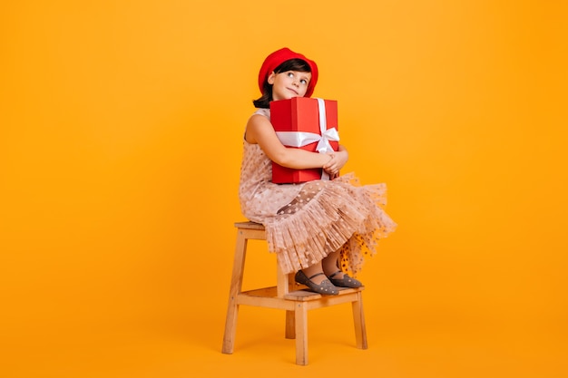 Happy brunette child sitting on chair with present.  little birthday girl wears cute dress.