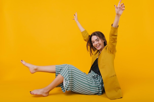 Free photo happy brunette girl in trendy pants expressing positive emotions during studio photoshoot indoor photo of dreamy young lady isolated on yellow background