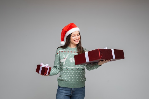 Free photo happy brunette santa girl in warm winter sweater with xmas and new year gifts on gray background with copy space