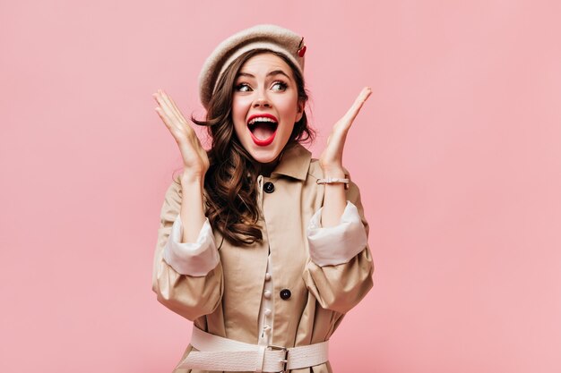 Happy brunette woman with red lips screams for joy on pink background.