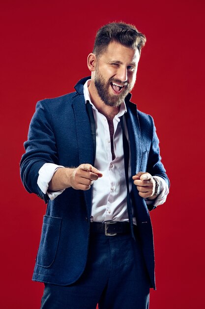 The happy business man point you and want you half length closeup portrait on red wall