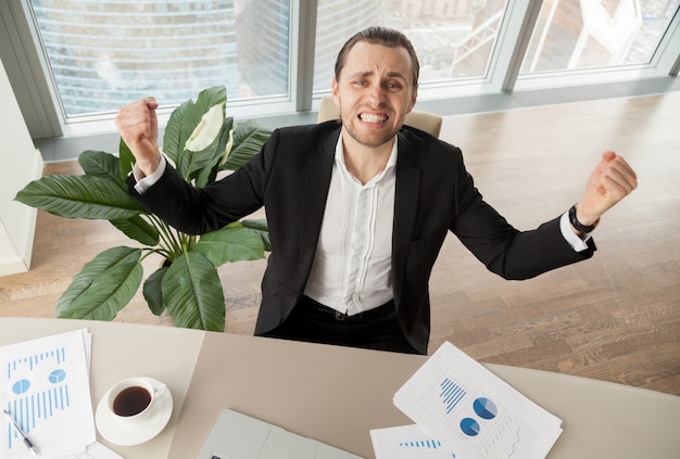 Free photo happy businessman at desk celebrating achievements