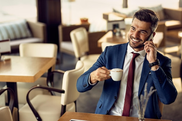 Happy businessman drinking coffee and talking on the phone in a cafe