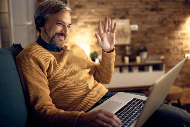 Happy businessman greeting someone during video call from home at night