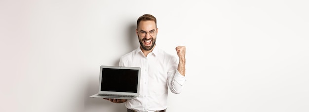 Free Photo happy businessman showing laptop screen make fist pump and rejoicing on online achievement standing