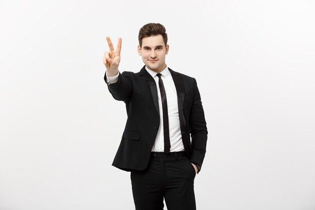 Happy businessman showing two fingers or victory gesture, against grey background. Success in business, job and education concept. Blank copyspace area for advertisiment, slogan or text