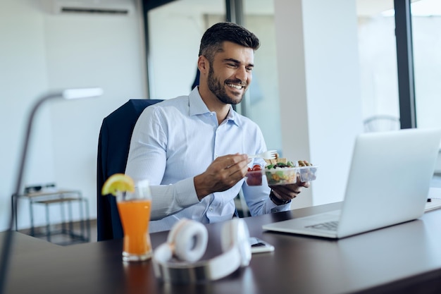 Happy businessman using laptop while having lunch break in the office