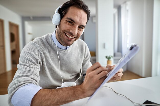 Happy businessman with headphones working on paperwork at home and looking at the camera