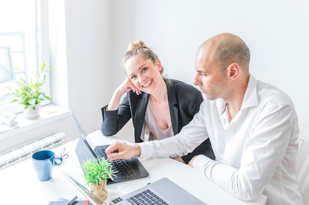 Free Photo happy businesswoman sitting with her colleague working on laptop