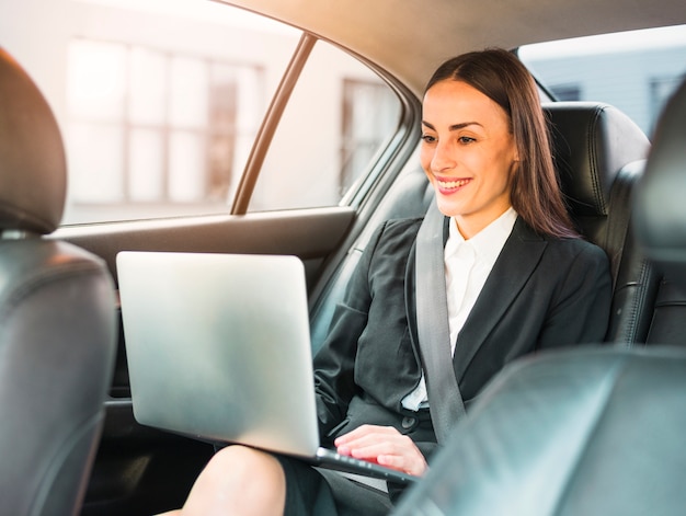 Happy businesswoman traveling by car using laptop