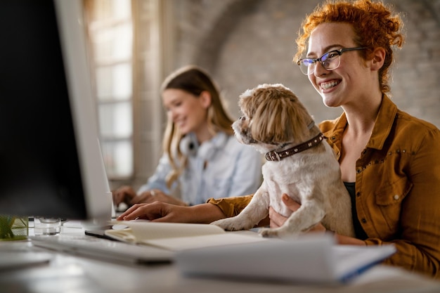 Happy businesswoman working on desktop PC while holding her dog in the office