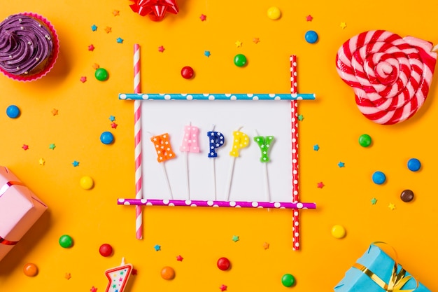 Happy candle with muffins; gems; sprinkles; gift boxes and heart shape lollipop on an orange backdrop