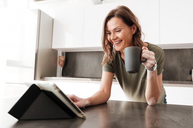 Happy Casual woman drinking coffee and using tablet computer on kitchen