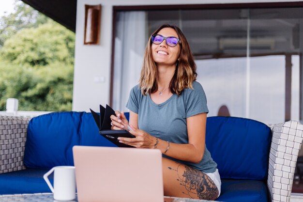 Happy caucasian woman does distance work on laptop at home comfortable place drinking tea